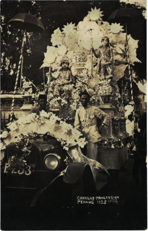 Black-and-white photo of a parade float adorning a car, with two men and two girls riding it.