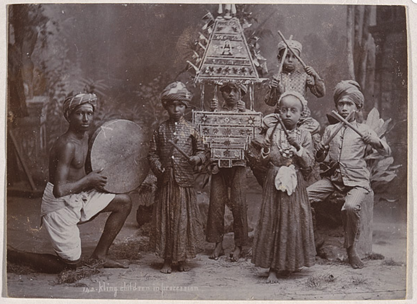 A posed group of six children. They are holding instruments and decorative items.