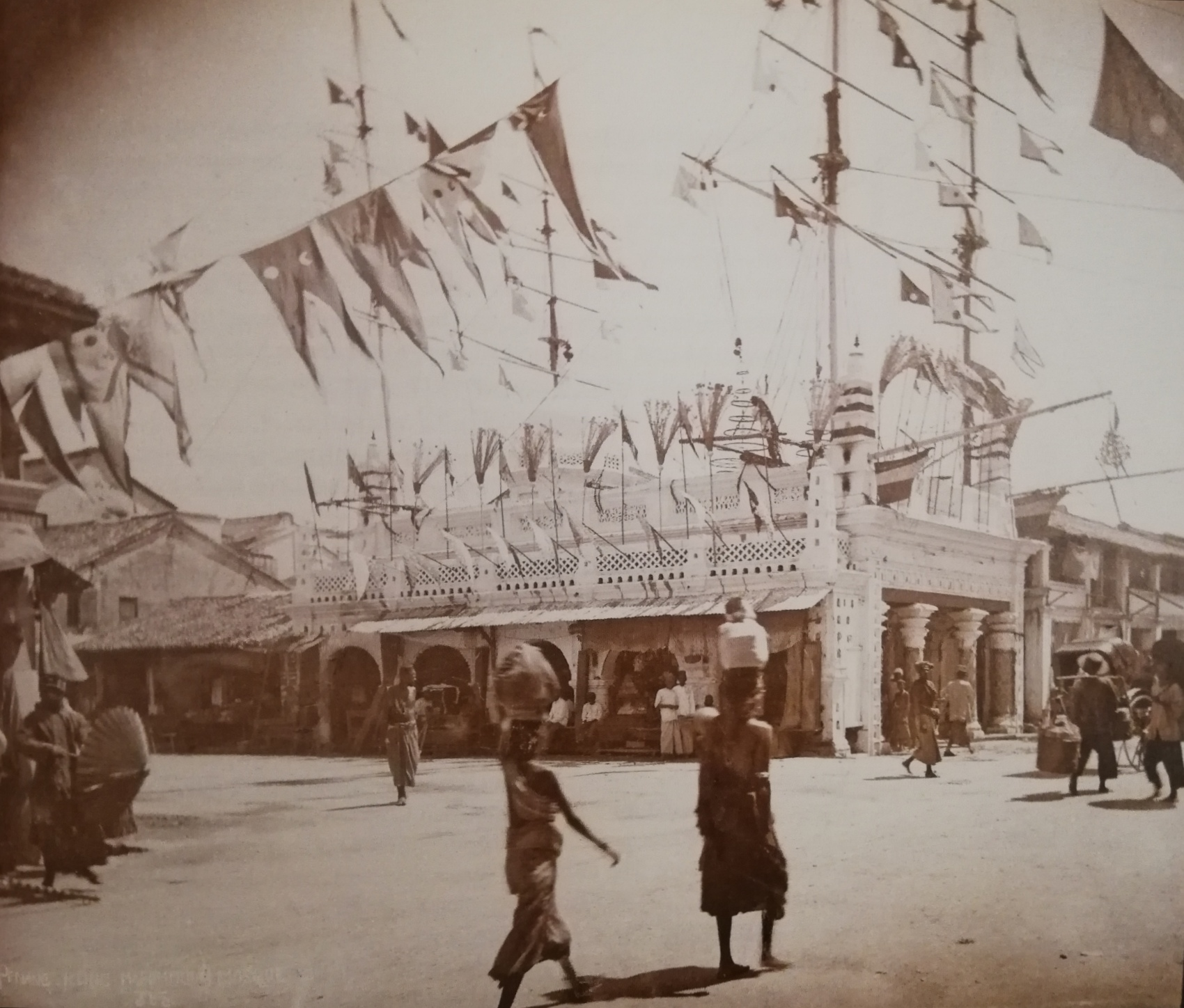 Sepia photo of the shrine with flags erected. People are moving about the street outside.