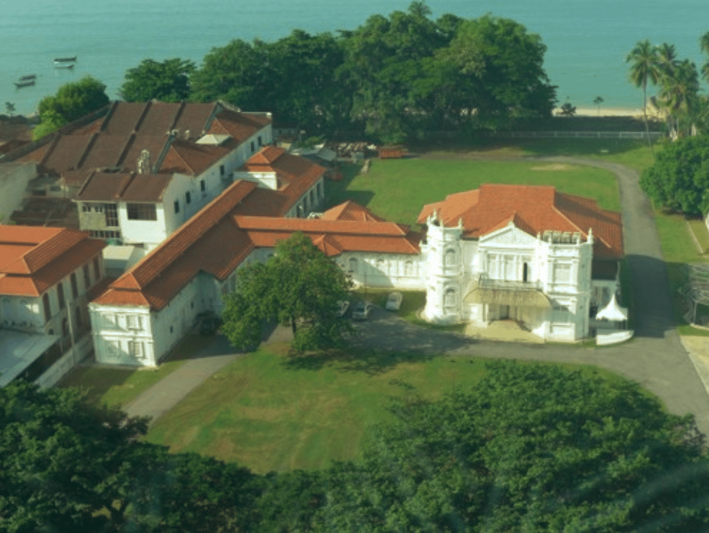 An aerial photo of Northam Lodge, a large mansion with white walls and a red roof. The mansion is by the water.