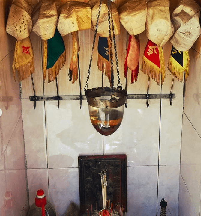 A shrine with flags and incense, as well as a hanging receptacle with liquid in it.