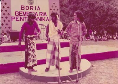 Three men singing on a small stage at a festival.