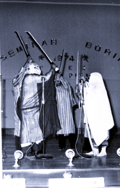 Black and white image of performers in costume with props.