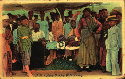 A colourised photo of two Malay 'dancing girls' surrounded by a group of boys and men.