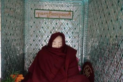 A monk with their lower face covered by their red robes.