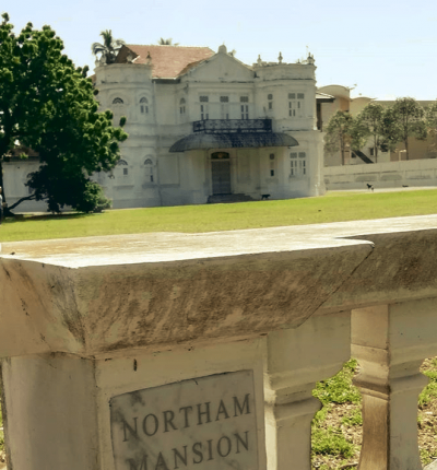 The sign on the property entrance to Northam Mansion, with the house seen over the fence in the background.