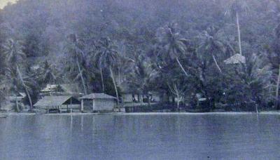 A black and white photograph of a camp built among the trees by the water.