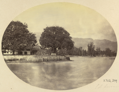 Black and white photo of a waterway banked by grass and trees.