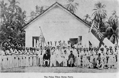 Black and white photo of members of the Pulau Tikus Borea Party in front of a mosque. They are holding British flags.