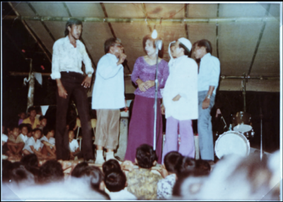 Colour photo of four performers singing in front of seated crowd.